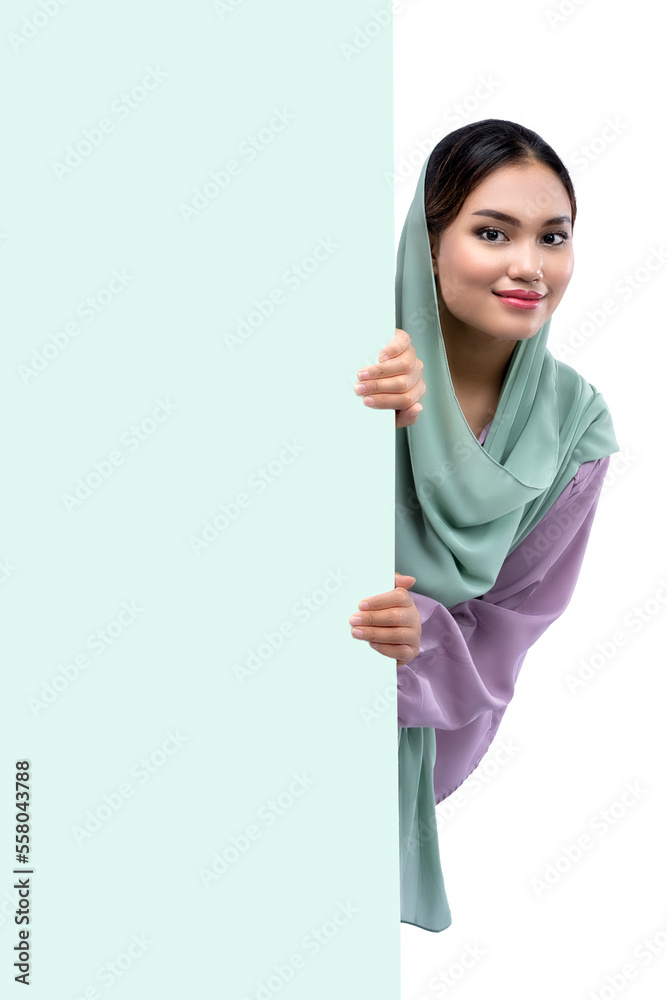 Asian Muslim woman in a headscarf standing behind an empty wall Asian Muslim woman in a headscarf standing behind an empty wall