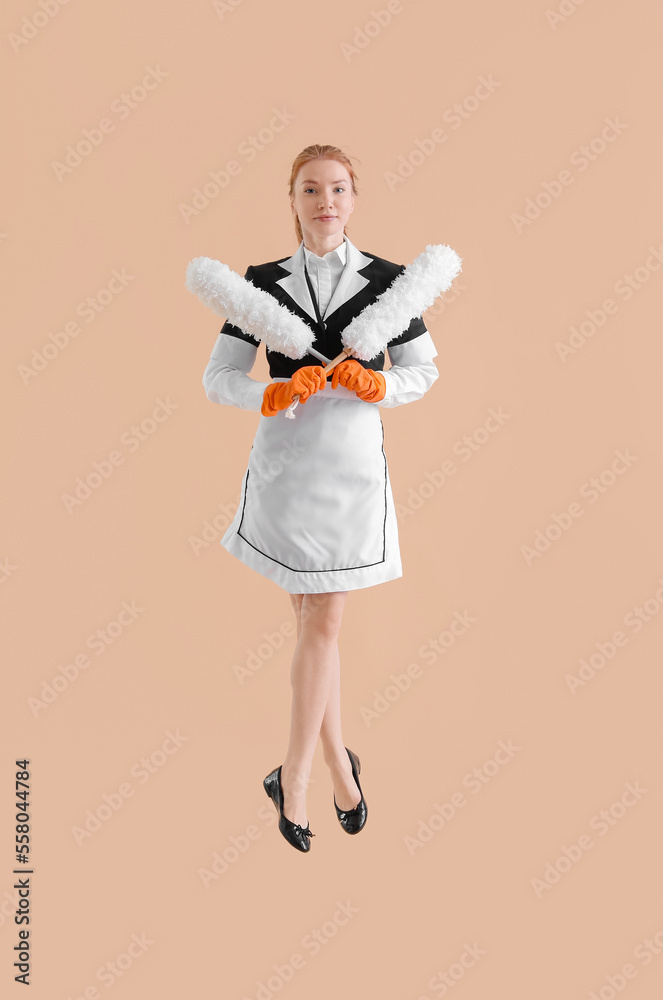 Fototapeta premium Young female chambermaid with dusters jumping on beige background