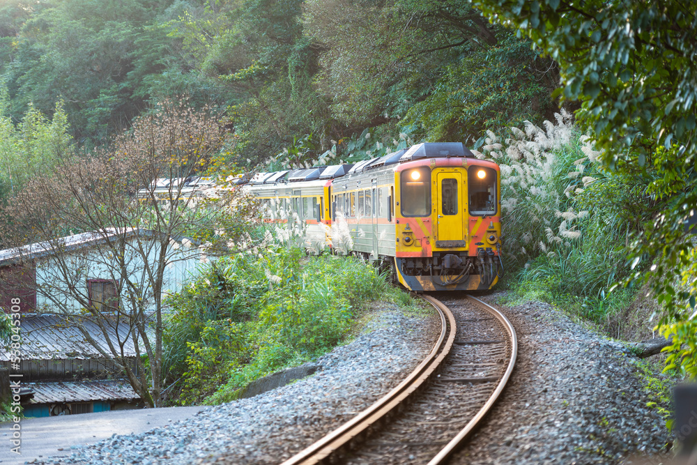 Naklejka premium Diesel yellow train travels in the mountains and forests. Sandiaoling Railway Station, Ruifang District, New Taipei City, Taiwan