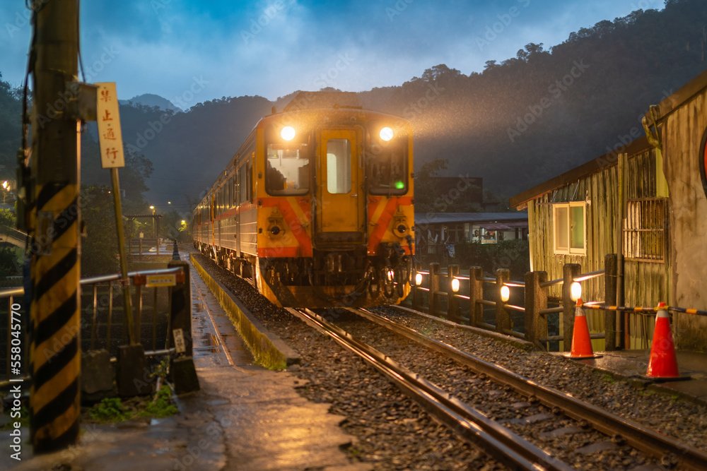 Trains with lights on are moving in the rain. Sandiaoling Railway Station, New Taipei City, Taiwan.  Translation 