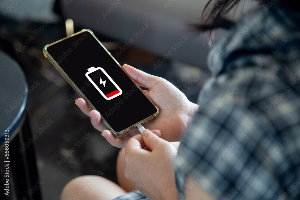Φωτογραφία Close up a woman holding a smartphone connected to a charger, displaying a low battery symbol on the screen