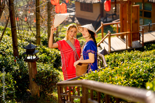 Two of pretty Asian women stand on stair along the way down from hill and posture for taking picture in place of travel landmark in Thailand.