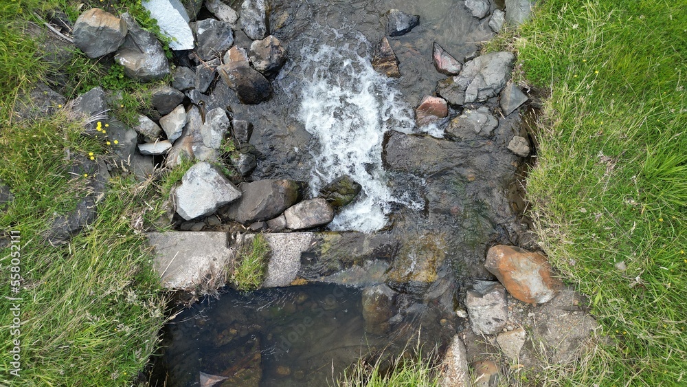 Obraz premium Water feature with rocks and grass surrounding the water. 