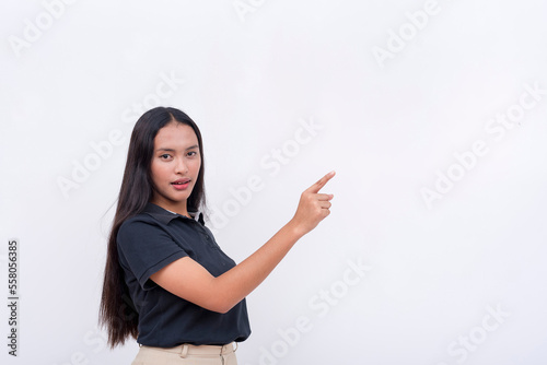 A pretty and young asian woman wearing a black polo shirt points to the upper right with her finger. Endorsing a product or service. Isolated on a white background.