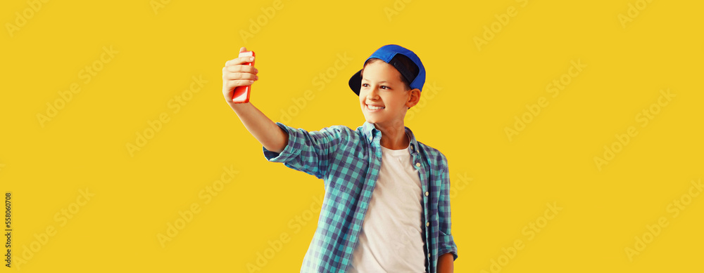 Portrait of happy smiling teenager boy taking selfie by smartphone on yellow background Portrait of happy smiling teenager boy taking selfie by smartphone on yellow background