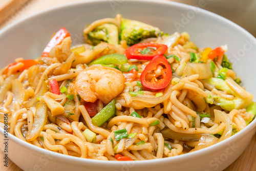 Golden coloured spicy sea food noodles with shrimp, broccoli, chilli pepper in a plate on wooden table