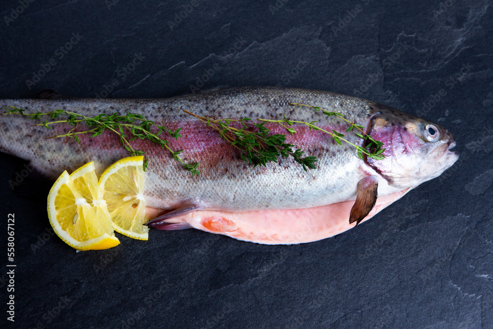 Fresh rainbow trout with spices and vegetables on black background. Cooking of sea food.