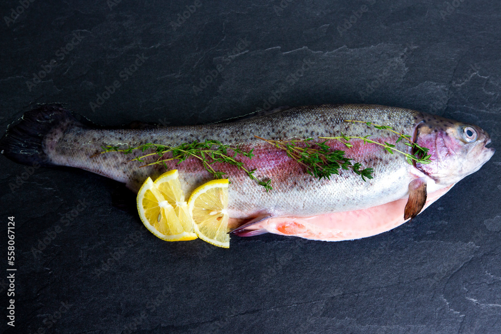 Rainbow trout with lemon and fresh thyme on black background. Mediterranean diet and cooking seafood.