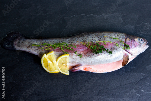 Obraz na płótnie Rainbow trout with lemon and fresh thyme on black background. Mediterranean diet and cooking seafood. w salonie
