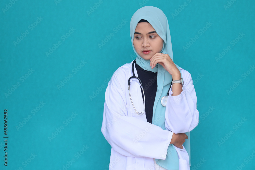 Female asian muslim wearing doctor coat and stethoscope with hand on chin thinking about question, pensive expression Female asian muslim wearing doctor coat and stethoscope with hand on chin thinking about question, pensive expression