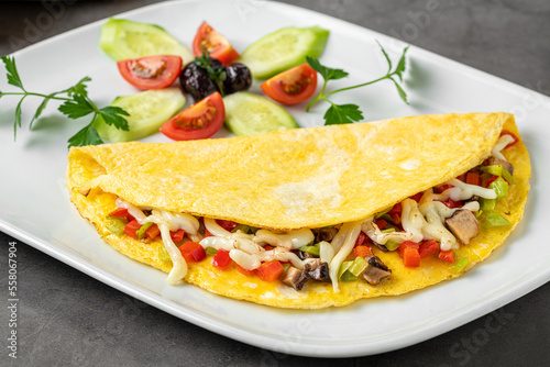 Omelet with cheese, mushrooms and vegetables on a white porcelain plate