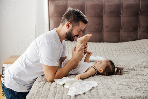 A caring father is changing his daughter's diapers and playing with her feet. photo