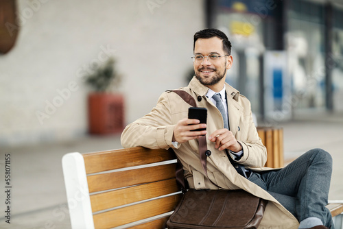 A stylish businessman in smart casual is sitting on a bench on a train station and waiting for a metro train.