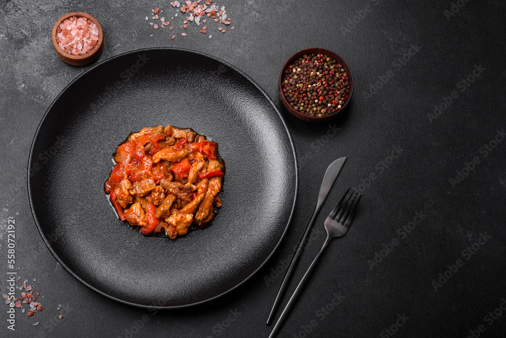 .Delicious juicy meat with hot peppers and sauce on a black ceramic plate