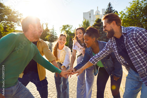Group friendly young multinational of people standing in circle stretching out hand forward enjoying outdoor team building activities feeling like friends with colleagues located on city street
