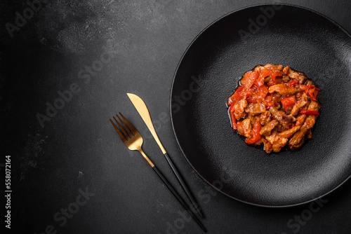 .Delicious juicy meat with hot peppers and sauce on a black ceramic plate