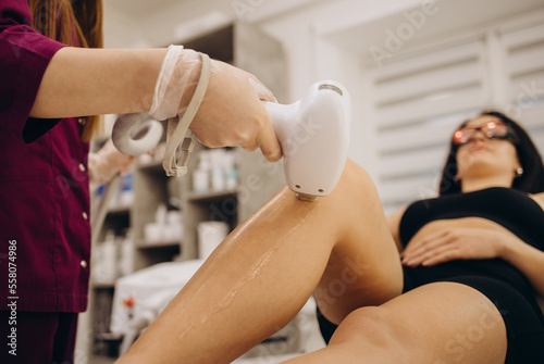 A master applies pink depilatory wax to a young woman's leg for hair removal. Depilation with wax. Beauty concept. Place for text. Selective focus.