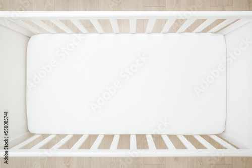 Empty baby crib with white mattress on wooden home floor. Closeup. Top down view.