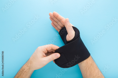 Young adult man hand putting protective black dark elastic wrist bandage on light blue table background. Pastel color. Top down view. Closeup. Point of view shot.