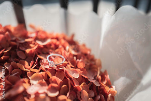 Close up of diamond ring on orange flower with sunlight and shadow background. Love, valentine, relationship and wedding concept. Soft and selective focus.