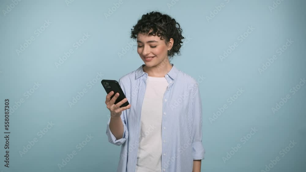 Young brunette woman wears blue shirt hold use mobile cell phone, swipe, browsing, doing online shopping, order delivery to home. Isolated on blue background studio Young brunette woman wears blue shirt hold use mobile cell phone, swipe, browsing, doing online shopping, order delivery to home. Isolated on blue background studio