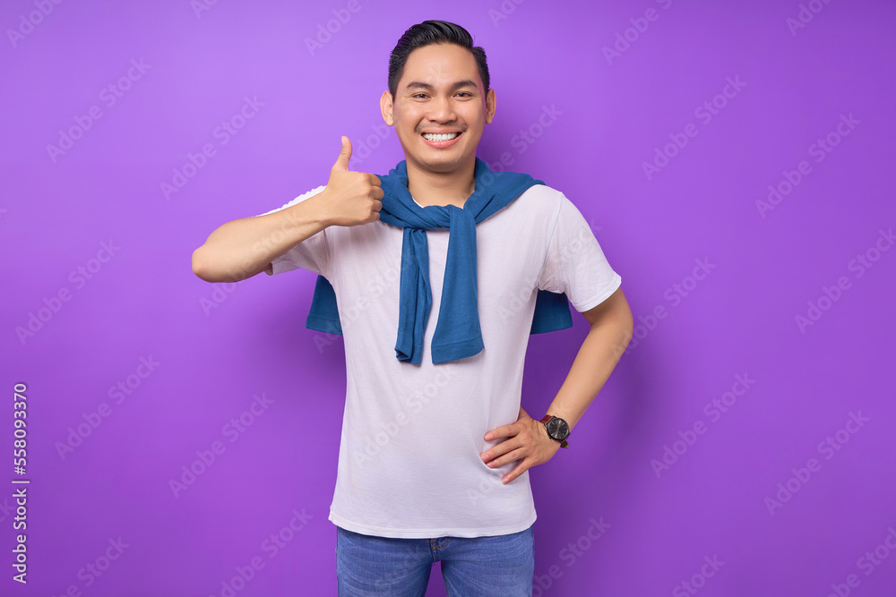 Smiling satisfied and cool young Asian man 20s wearing white t-shirt casual clothes showing thumbs up like gesture isolated on purple background. People lifestyle concept Smiling satisfied and cool young Asian man 20s wearing white t-shirt casual clothes showing thumbs up like gesture isolated on purple background. People lifestyle concept