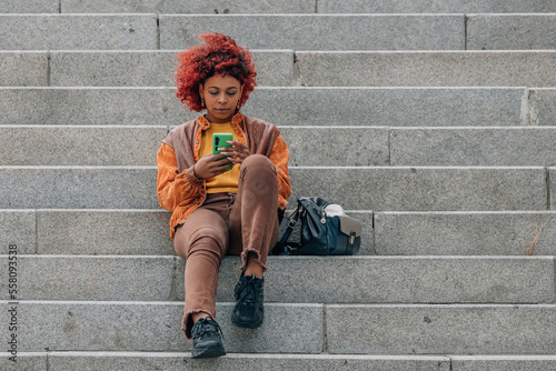 afro american girl on the stairs in the street with mobile phone
