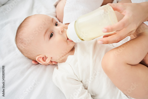 Cute little newborn boy eats milk from a bottle, a nipple.