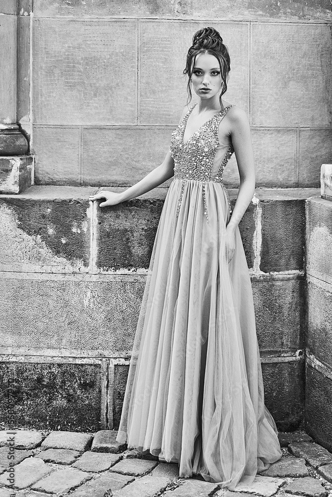 Beautiful bridesmaid lady in gorgeous elegant stylish floor length v neck chiffon gown dress decorated with sequins sparkles and rhinestones holding flowers bouquets. Wedding day in old beautiful