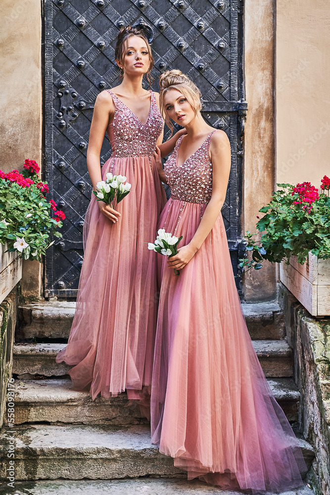 Beautiful bridesmaids in gorgeous elegant stylish red pink violet floor length v neck chiffon gown dress decorated with sequins sparkles and rhinestones holding flowers bouquets. Wedding day in old