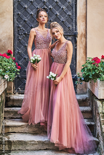 Obraz na płótnie Beautiful bridesmaids in gorgeous elegant stylish red pink violet floor length v neck chiffon gown dress decorated with sequins sparkles and rhinestones holding flowers bouquets. Wedding day in old w salonie