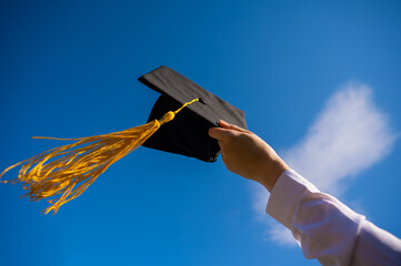 Close-up of a woman's hand with a graduation cap against the blue sky. 
