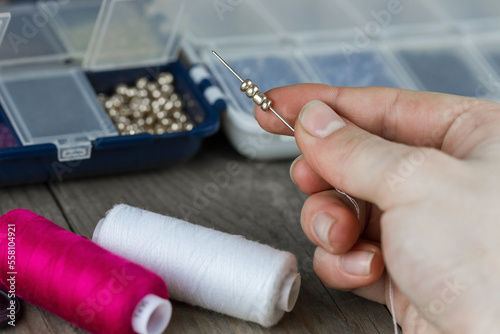Female hands making of handmade jewellery. Box with beads, spool of threads, needle on wooden background