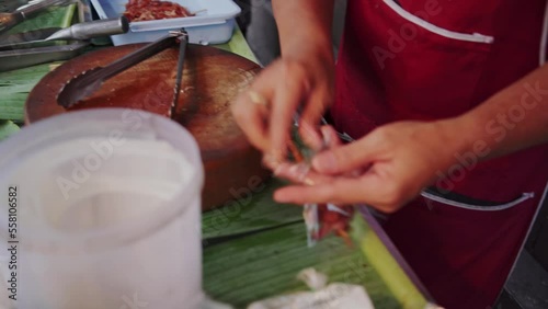 Street merchant putting Thai sun-dried pork (Moo Dad Deaw) skewer in a plastic bag