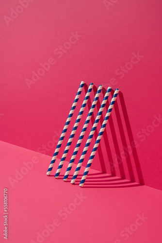 Blue striped paper straws leaning on magenta wall. Minimal concept.