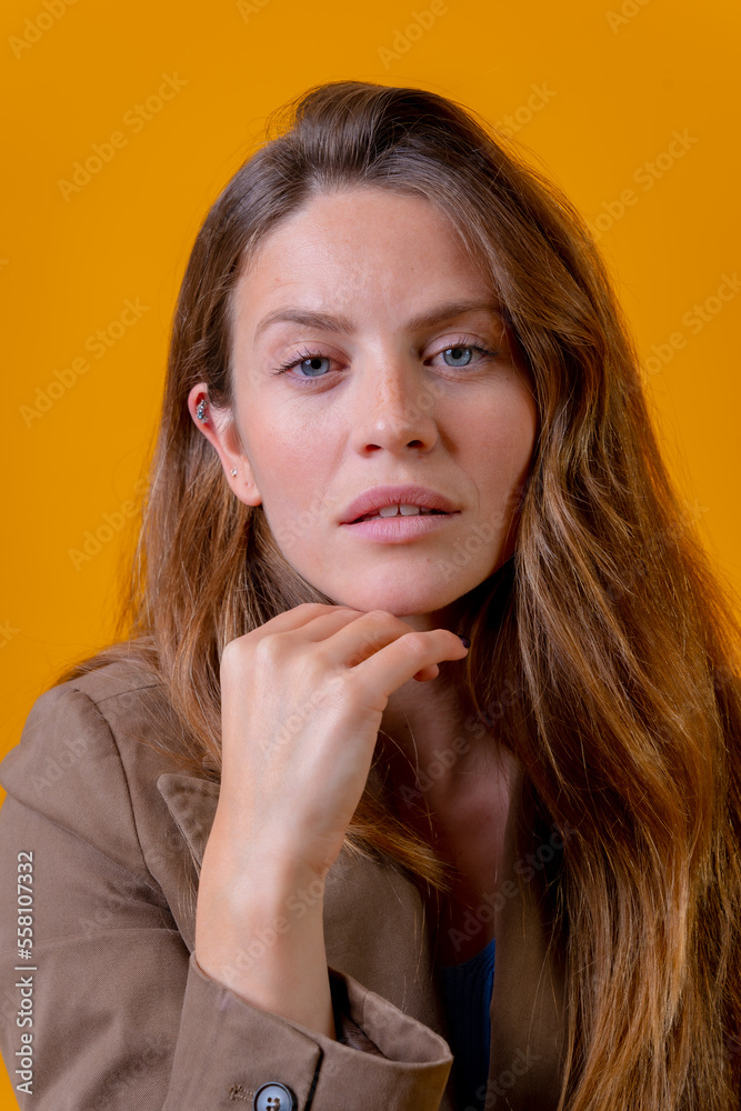 Portrait of attractive blue-eyed woman on a yellow background in a brown jacket looking at camera Portrait of attractive blue-eyed woman on a yellow background in a brown jacket looking at camera