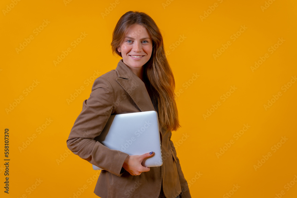 Fototapeta premium Portrait of a businesswoman with a computer on a yellow background, young entrepreneur concept