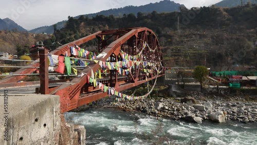 Kullu Manali Himachal Pradesh India. Buddhist prayer flags fluttering in the wind. Old Iron bridge over Beas river flowing through beautiful snow covered Indian mountain in Himalayas.  photo
