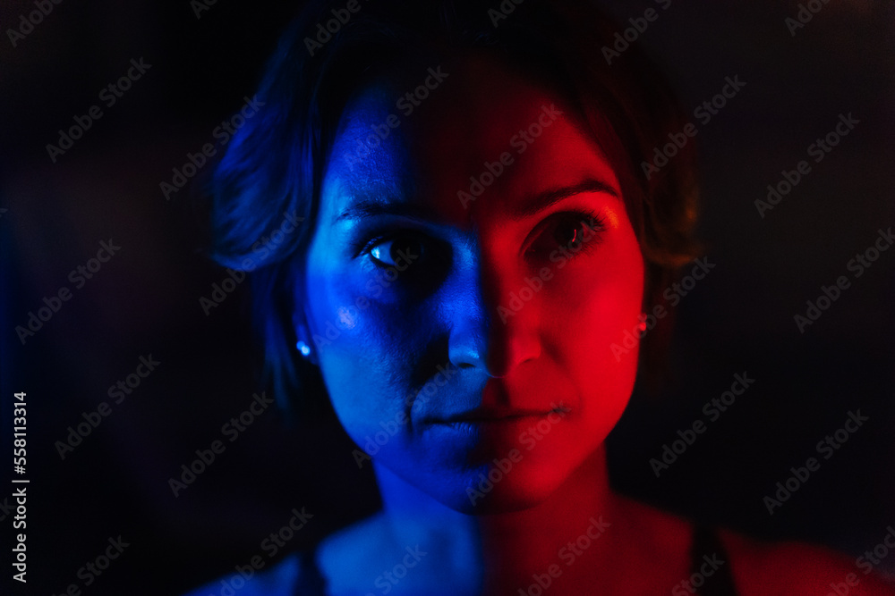 The face of a young woman in blue and red neon light on a dark background