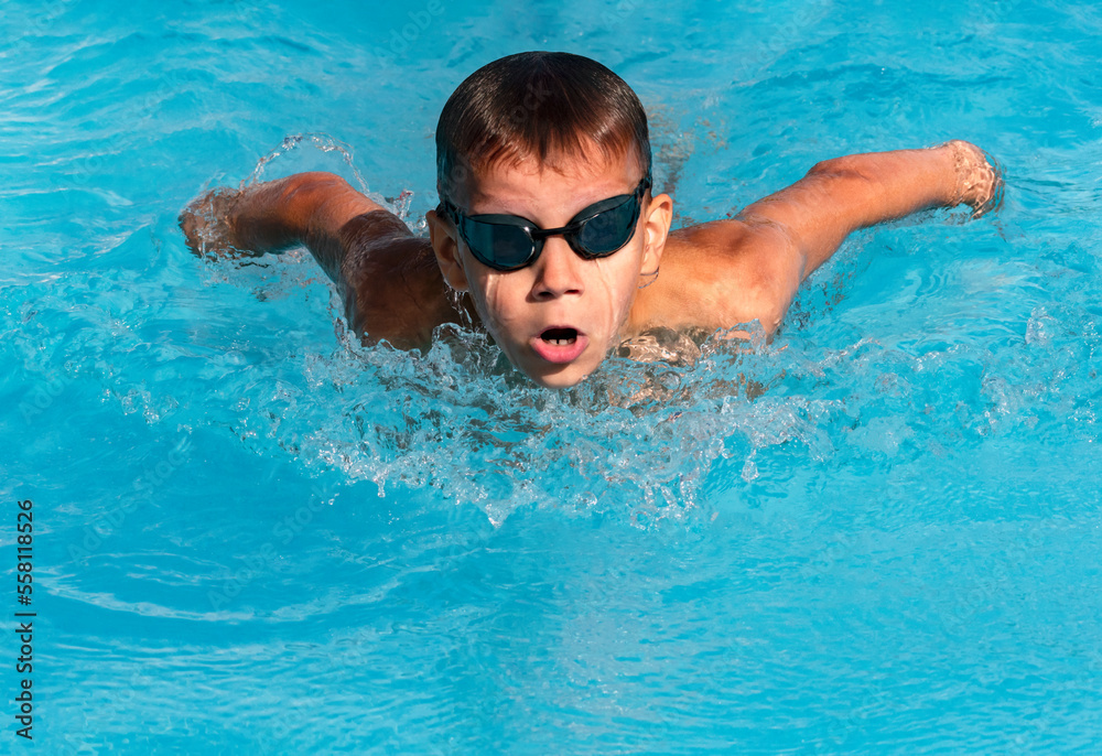 Boy swimmer swimming butterfly stroke in pool in action. Young athlete swim in swimming pool, training before competition. Water sports, learn to swim school classes for children