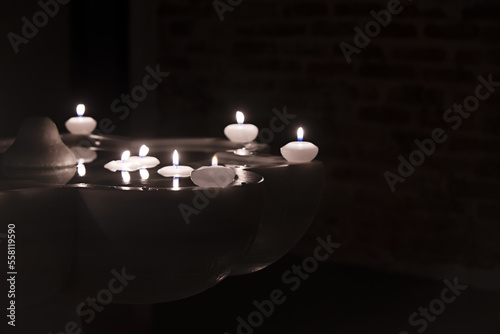 Floating wax candles burning in a marble fountain in the dark