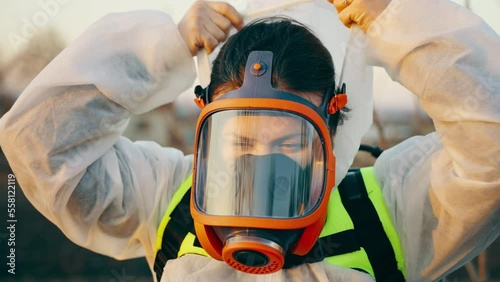 A garden worker in a respirator puts on a protective suit before picking trees