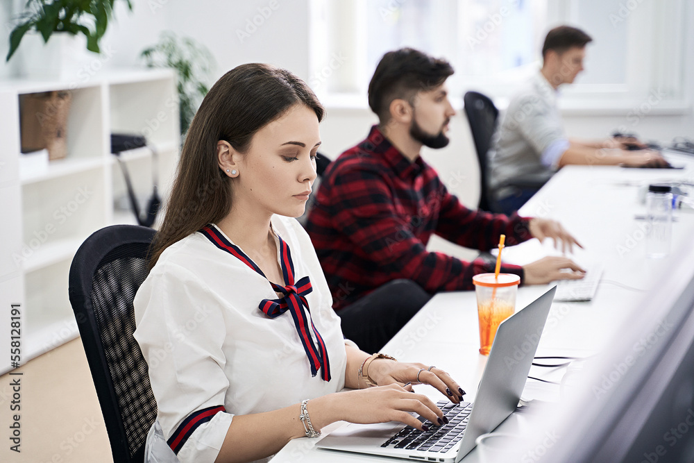 People working in modern IT office. Group of young and experienced programmers and software developers sitting at desks working on computers. Team at work. High quality image.
