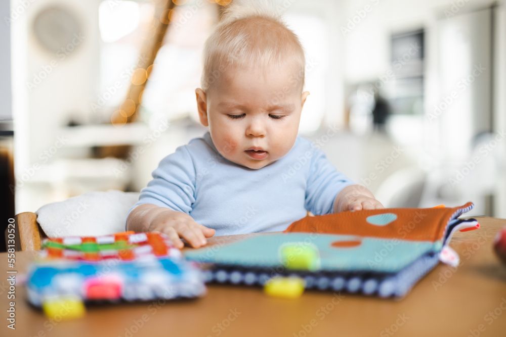 Happy infant sitting at dining table and playing with his toy in traditional scandinavian designer wooden high chair in modern bright atic home. Cute baby playing with toys. Happy infant sitting at dining table and playing with his toy in traditional scandinavian designer wooden high chair in modern bright atic home. Cute baby playing with toys.