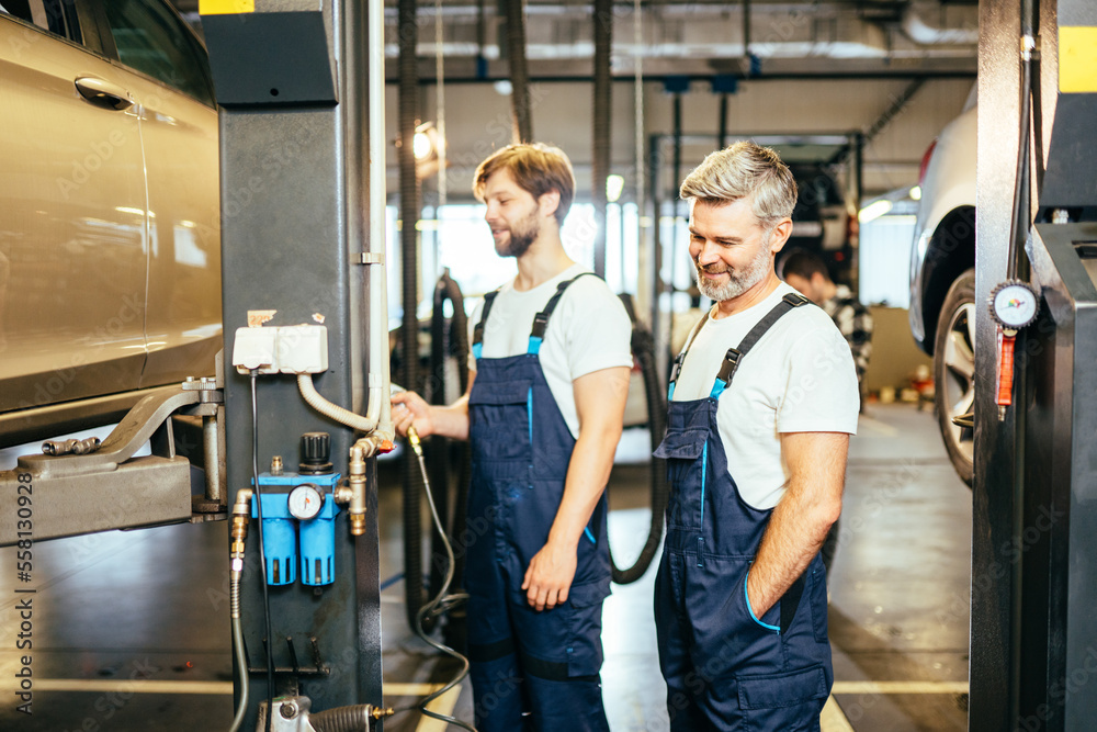 Obraz premium Father and son in uniform work at the auto service. Two garage technician men or two workers work together in front of car to maintenance and fix the problem.