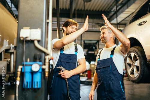 Father and son work at the auto service. Two mechanics giving high five during work with the details of the car. People occupation and business job.