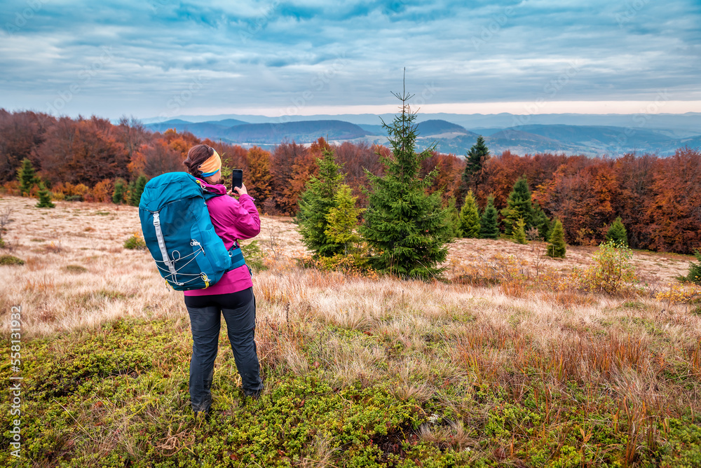 A tourist with a backpack takes pictures of the mountains on her phone