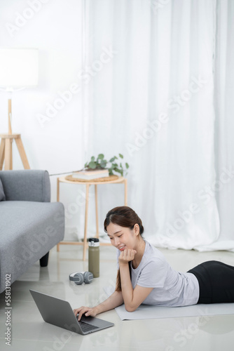 Young asian woman attractive exercises workout at home and watching Online sports tutorials over laptop