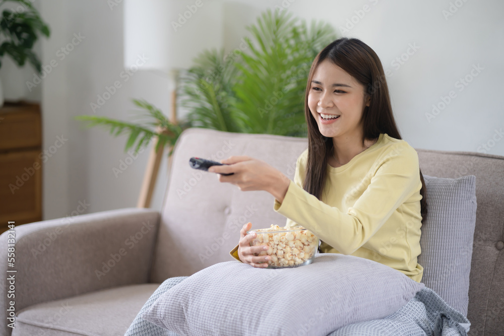 Asian girl relaxing at home using remote control and choosing TV show or movie. Enjoying Watching Television Asian girl relaxing at home using remote control and choosing TV show or movie. Enjoying Watching Television