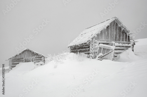 Two abandoned log cabins in winter foggy mountains